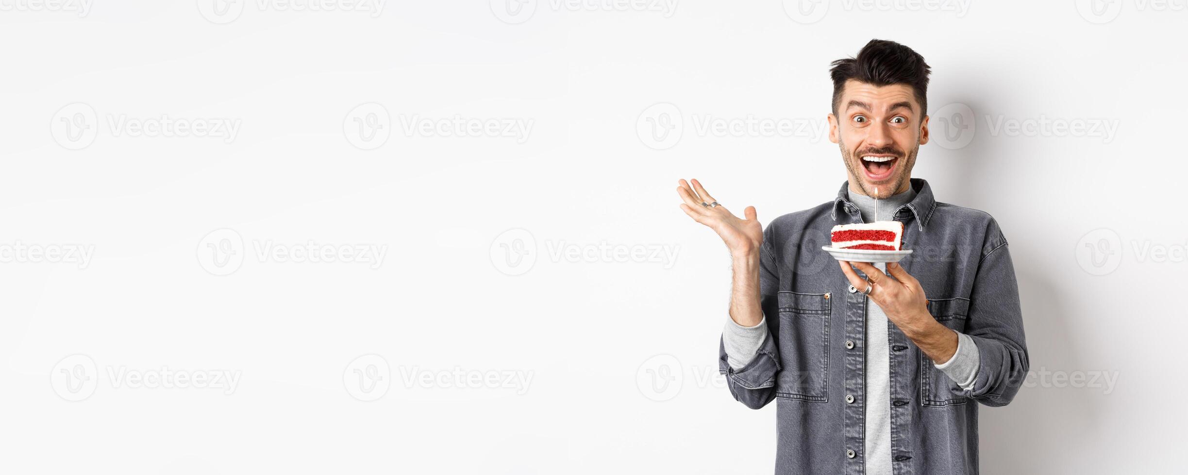 Excited man celebrating birthday, looking happy, holding cake with candle, making wish, standing happy against white background photo