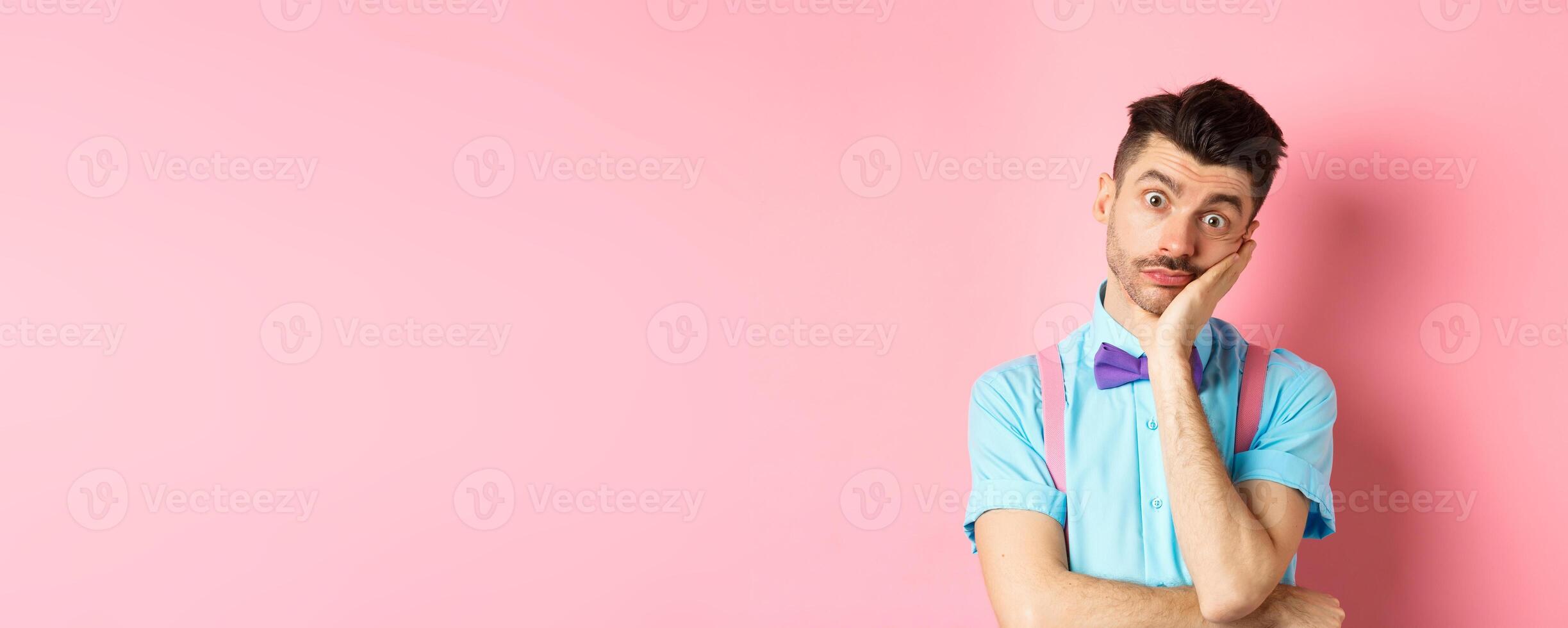 Shocked and tired caucasian guy staring pissed-off at camera, lean on palm and looking at something with skeptical face, standing over pink background photo