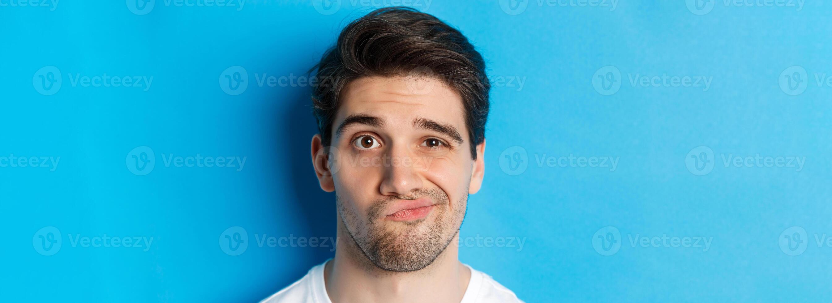 Headshot of skeptical guy looking at something unamusing, grimacing and standing reluctant against blue background photo
