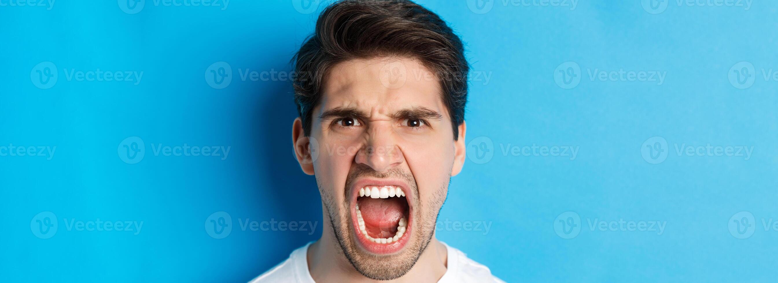 Head shot of angry man shouting and looking with hatred, standing mad against blue background photo