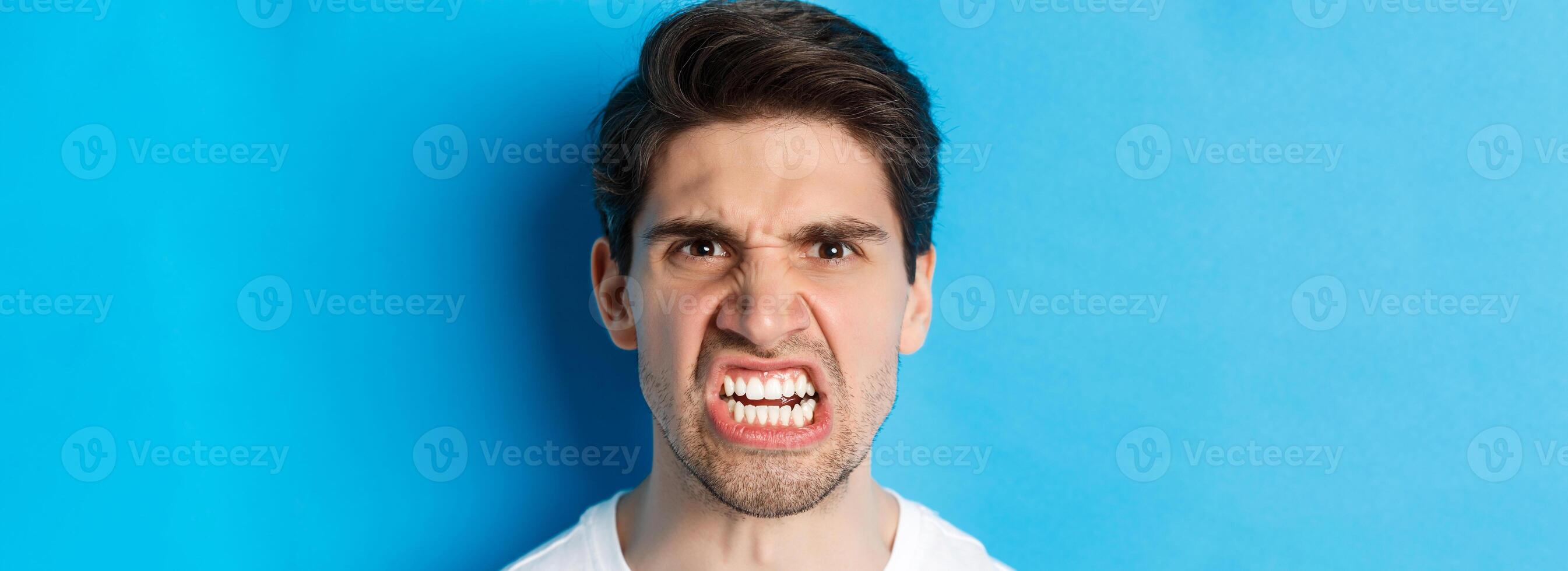 Headshot of angry caucasian man looking with scorn and dismay, being mad at person, standing against blue background photo