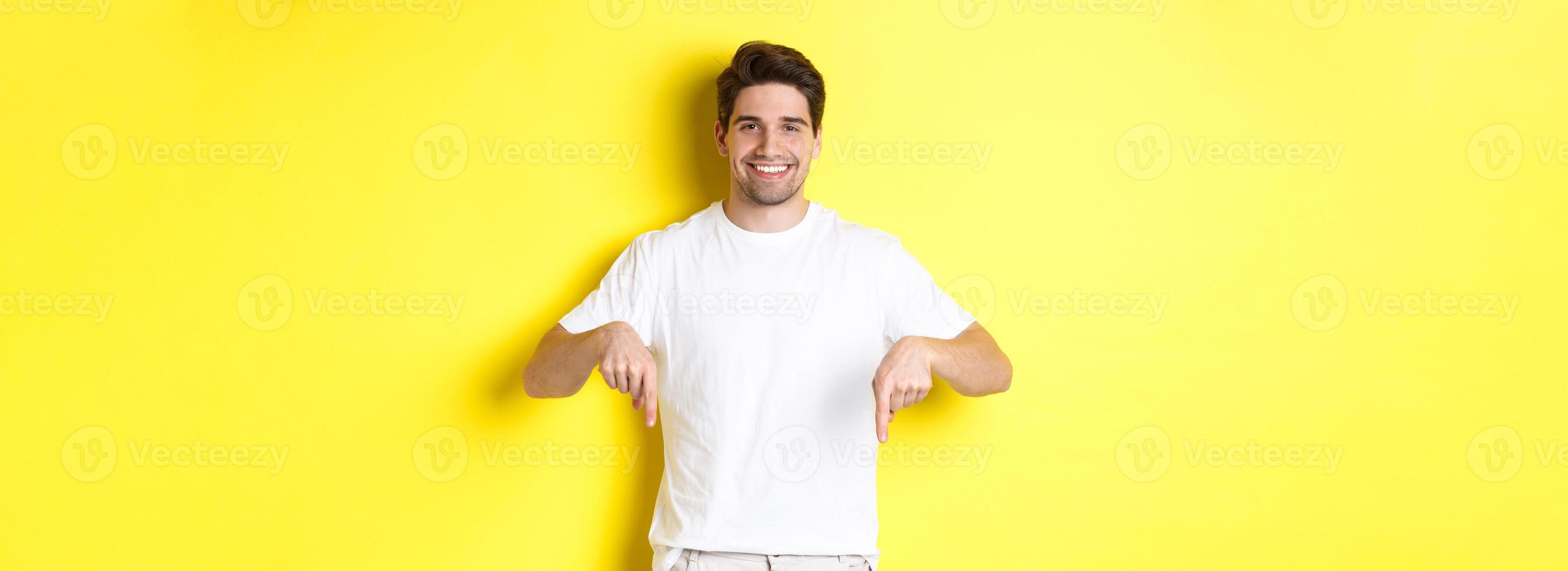 Attractive bearded man pointing fingers down, showing event banner, standing over yellow background photo