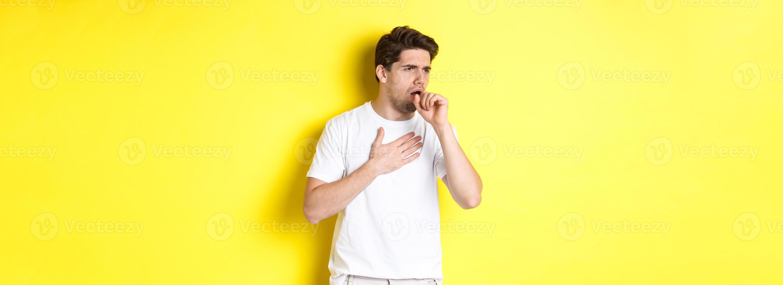 Image of man with covid-19 or flu symptoms, coughing and feeling sick, standing over yellow background photo