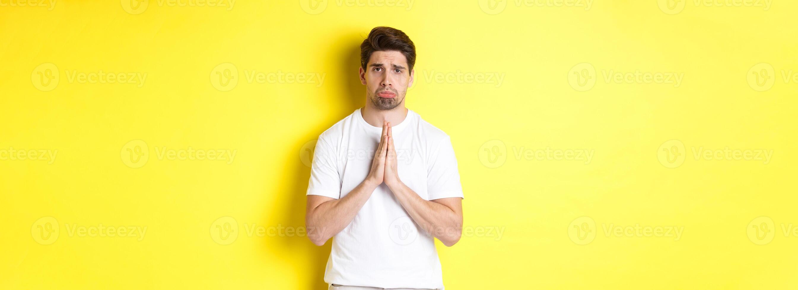 Sad guy begging for something, sulking and asking for favour, saying sorry, standing over yellow background photo