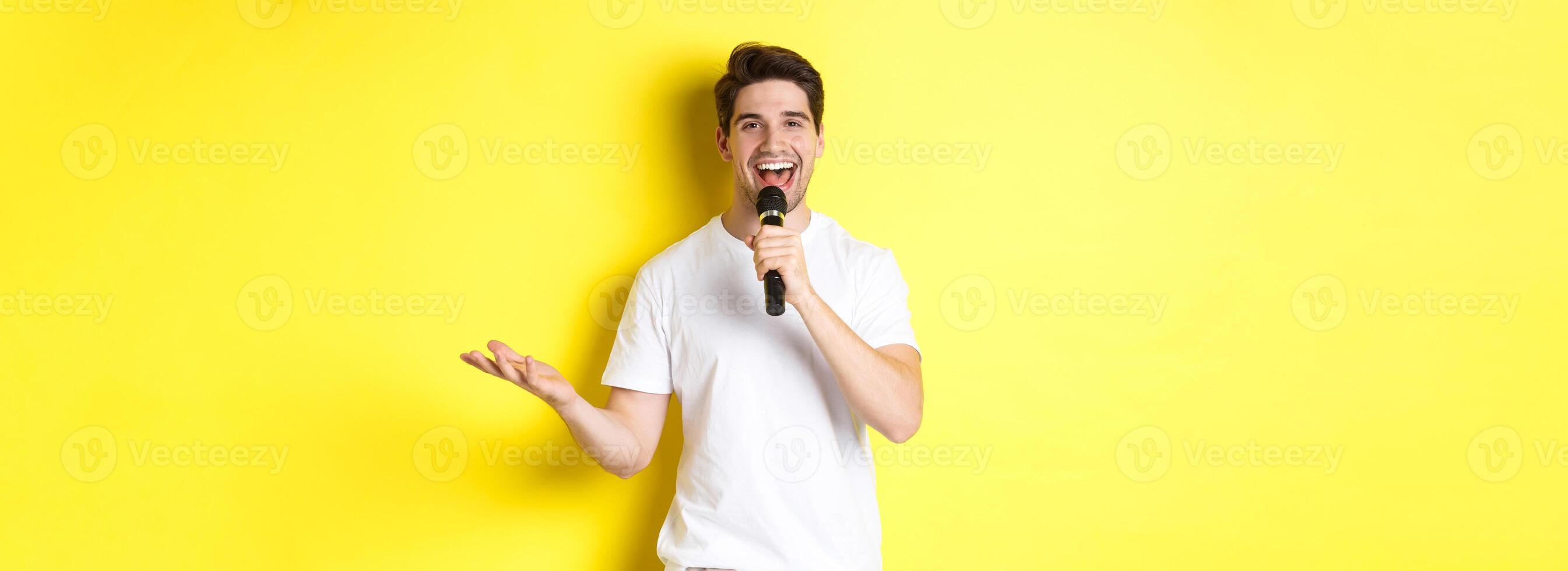 Happy man entertainer performing, talking in microphone, making speech or stand-up show, standing over yellow background photo