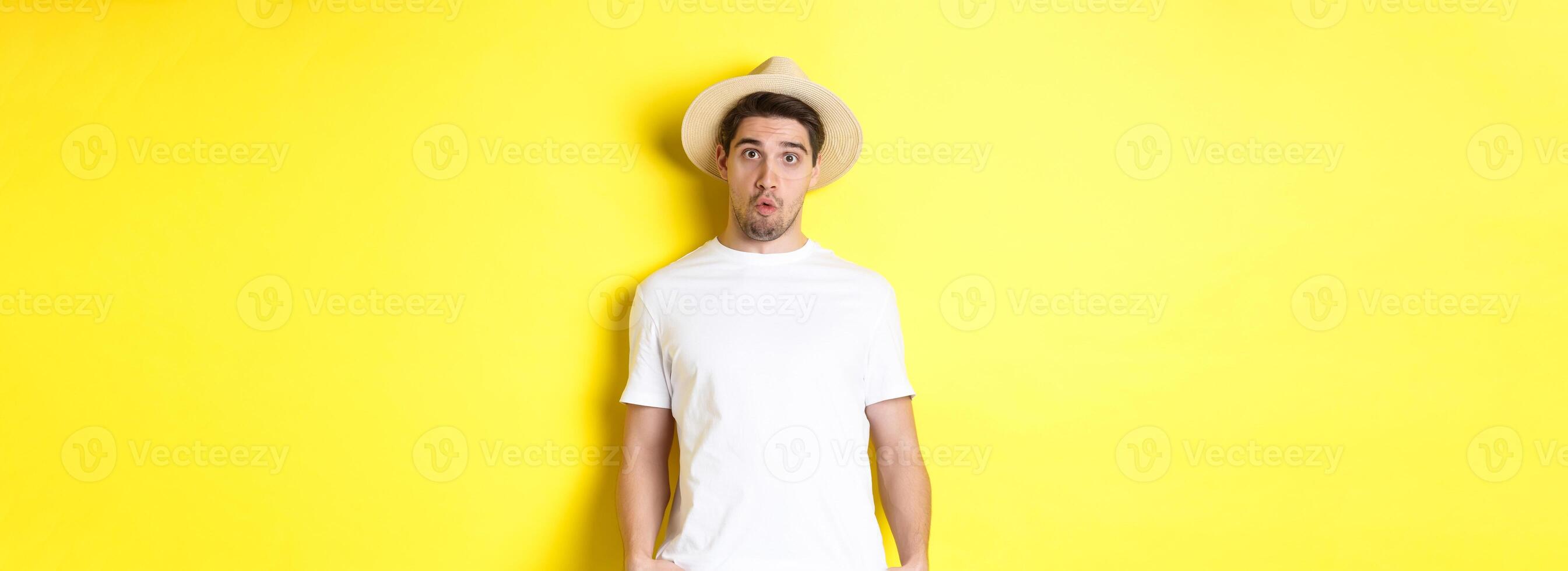 Confused guy traveller in straw hat looking puzzled, stare at camera, standing over yellow background photo