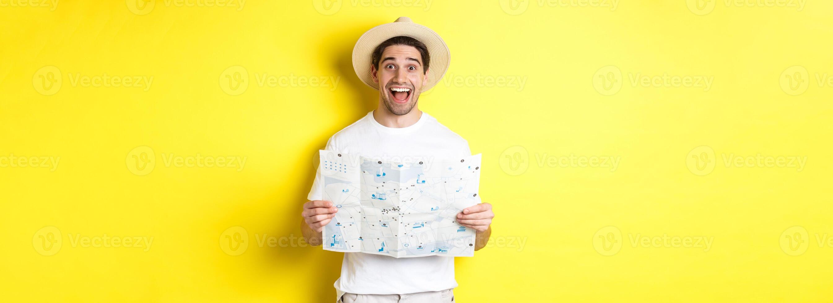 Travelling, vacation and tourism concept. Excited man tourist going sightseeing with map, standing over yellow background photo