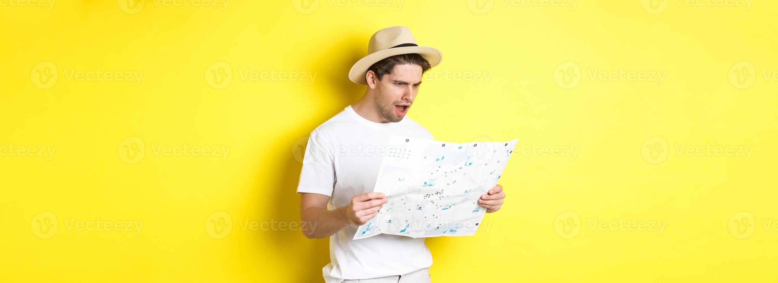 Travelling, vacation and tourism concept. Tourist looking displeased and shocked at road map, standing against yellow background photo