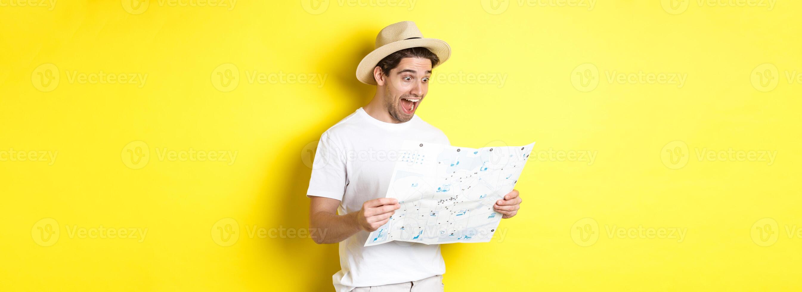 Travelling, vacation and tourism concept. Smiling happy tourist looking at map with sightseeings, standing against yellow background photo