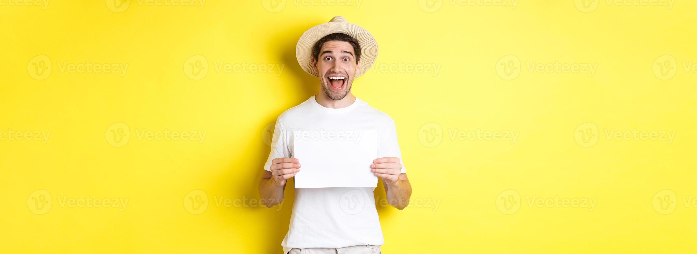 Excited tourist showing your logo or sign on blank piece of paper, smiling amazed, standing against yellow background photo