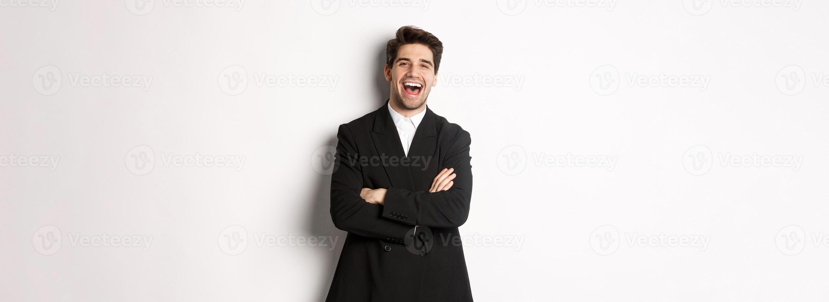 Portrait of attractive adult man in suit laughing and looking happy, standing in suit with hands crossed over chest, posing against white background photo