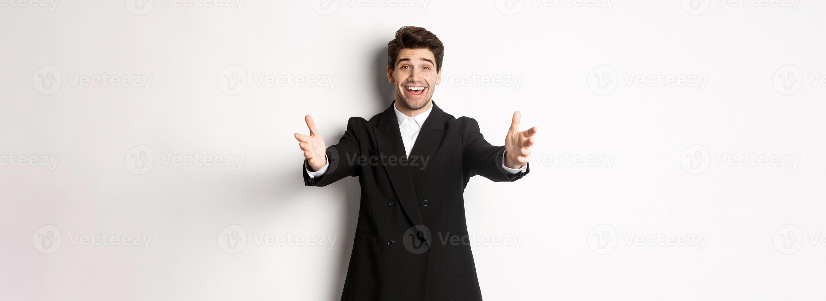 Portrait of happy attractive man in suit, hosting a party, reaching hands forward to greet you, want to hold something or hug, standing over white background photo