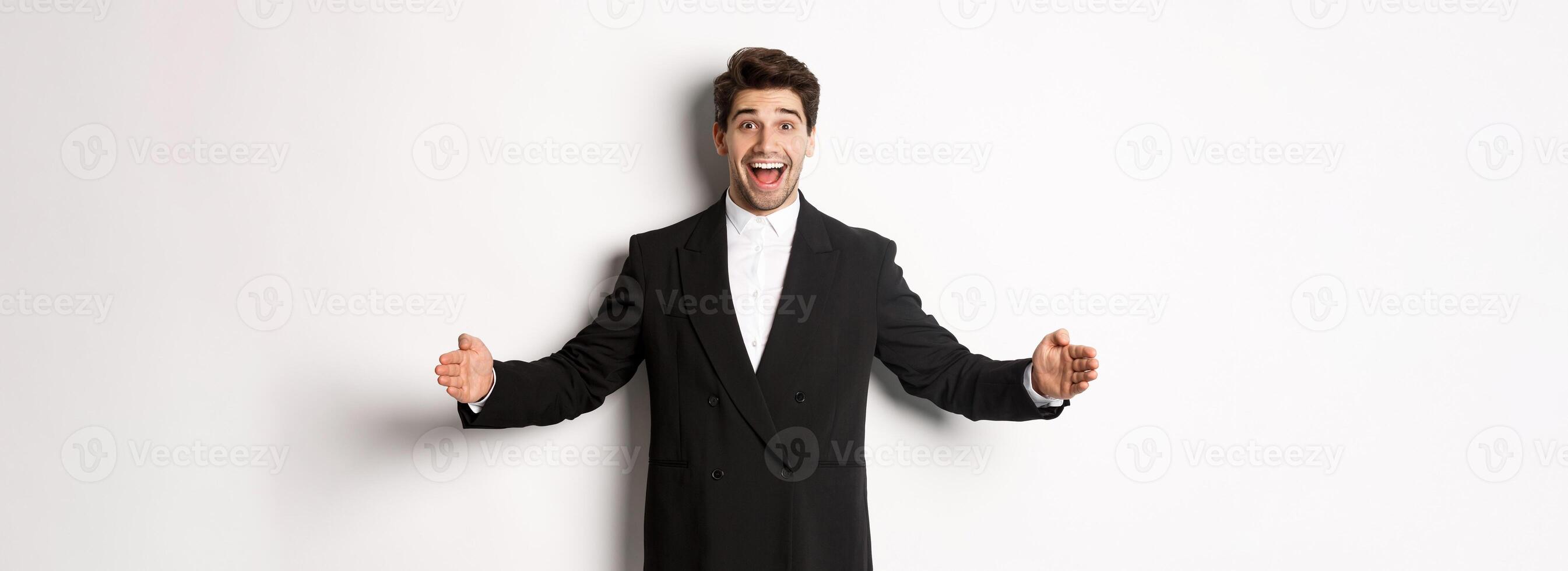 Portrait of excited handsome man in suit, shaping big object on copy space and smiling amazed, holding something, standing over white background photo
