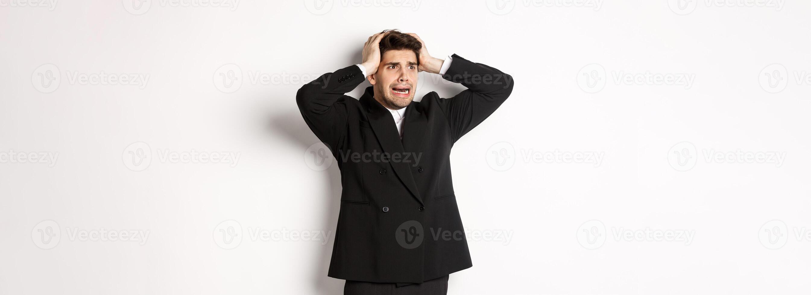 Image of anxious businessman start to panic, looking left with worried expression, standing in black suit over white background photo