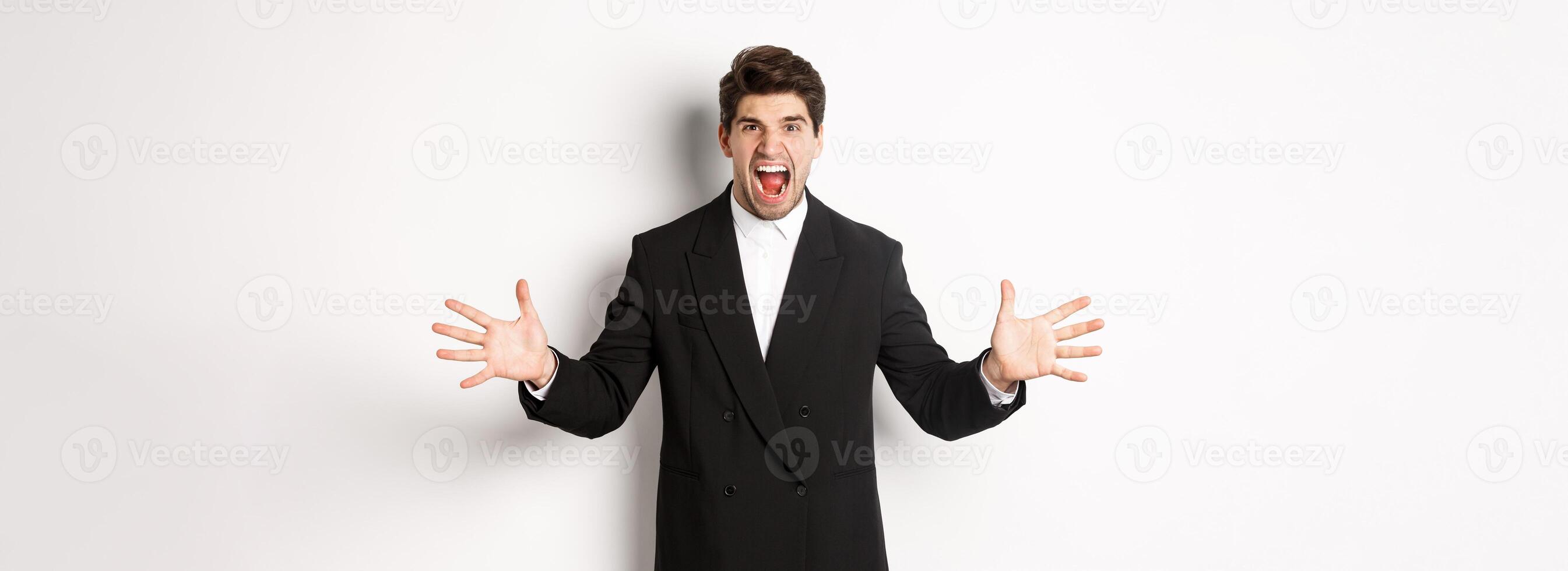 Portrait of pissed-off and frustrated businessman in suit, shouting angry and shaking hands, standing distressed against white background photo