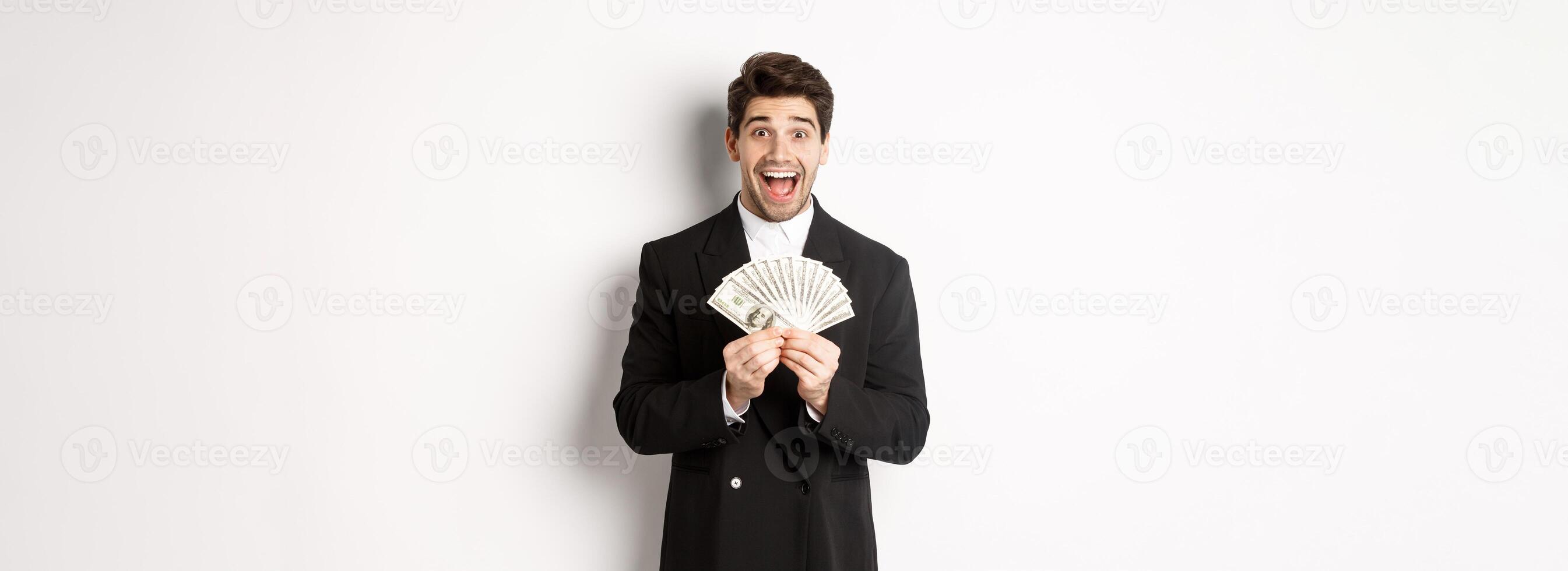 Portrait of handsome successful businessman in trendy suit, showing money and smiling amazed, earn cash, standing over white background photo