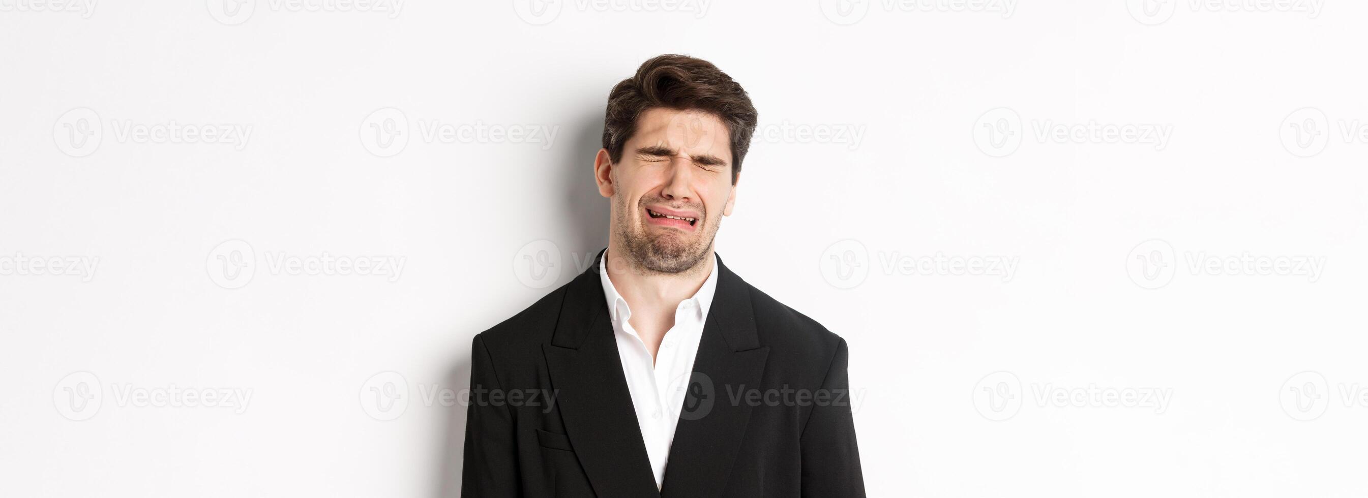 Close-up of miserable man in suit, crying and sobbing, feeling sad, standing against white background photo