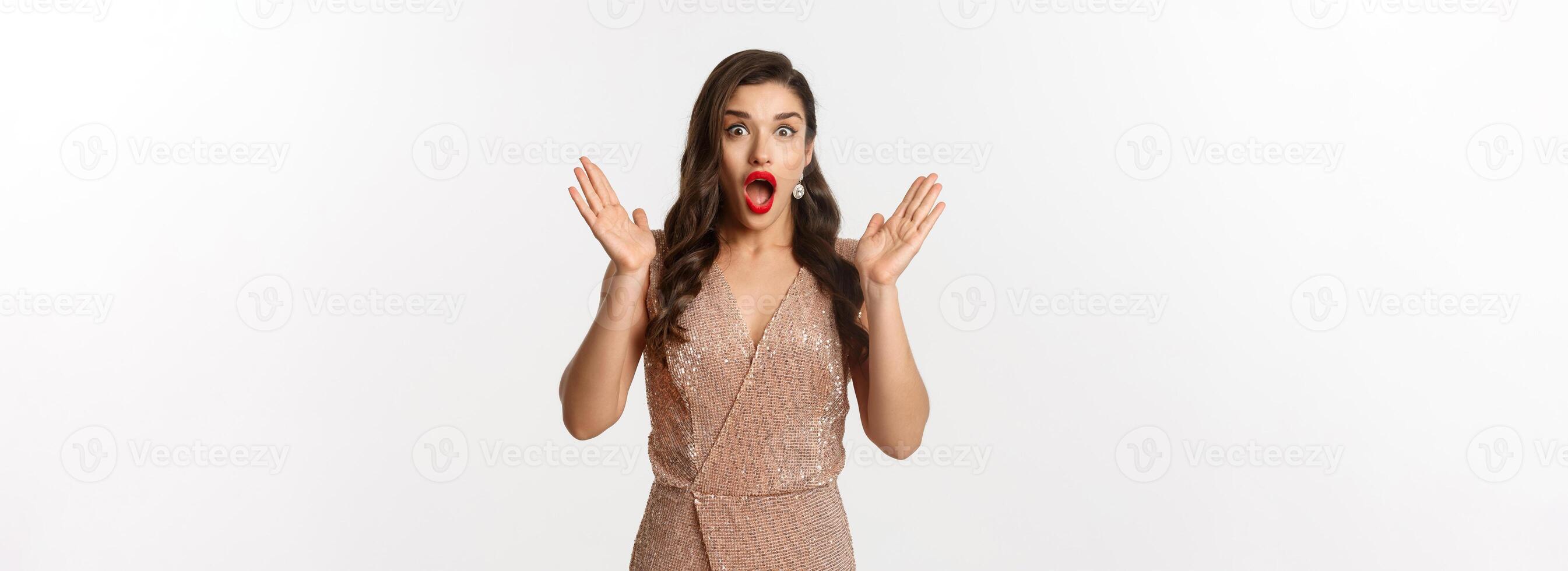 Winter holidays. Beautiful woman in evening dress and makeup, looking surprised and impressed at camera, stare at New Year promo offer, white background photo