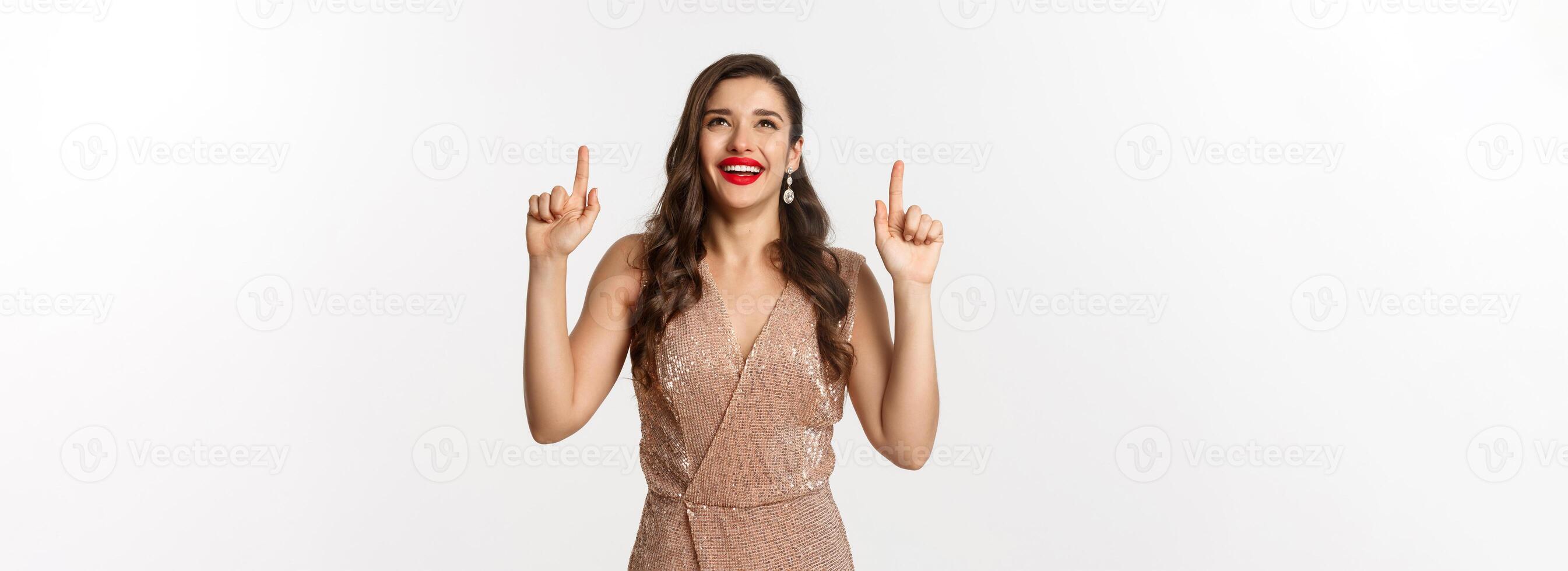 New Year, christmas and celebration concept. Happy elegant woman in party dress, laughing and looking up, pointing at top promo offer, white background photo