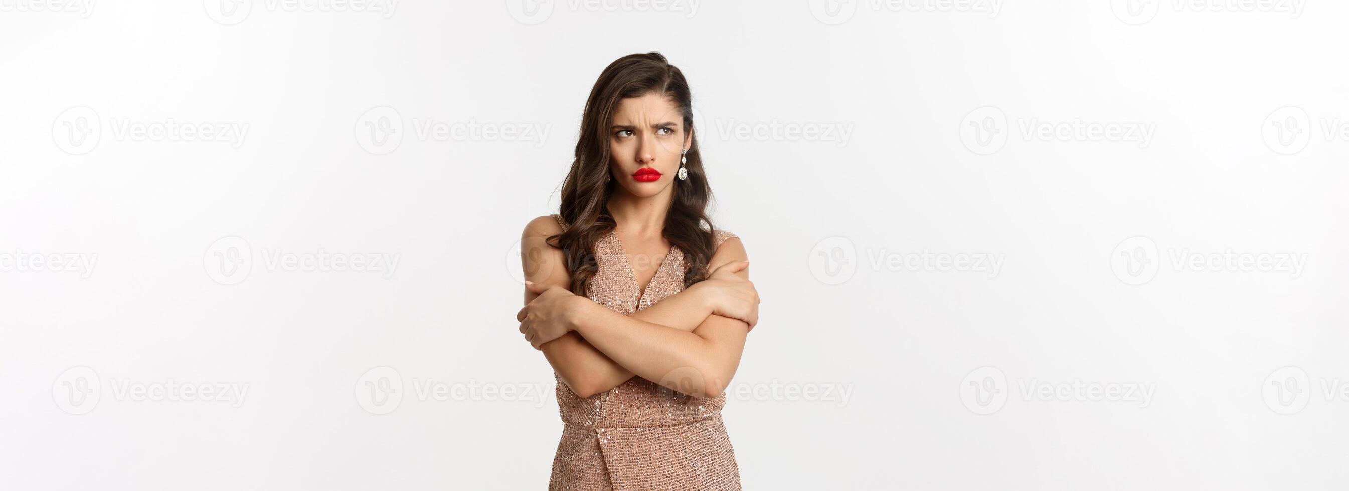 Celebration and party concept. Sulking woman looking angry, dressed for formal event in glamour dress, hugging herself and pouting upset, white background photo