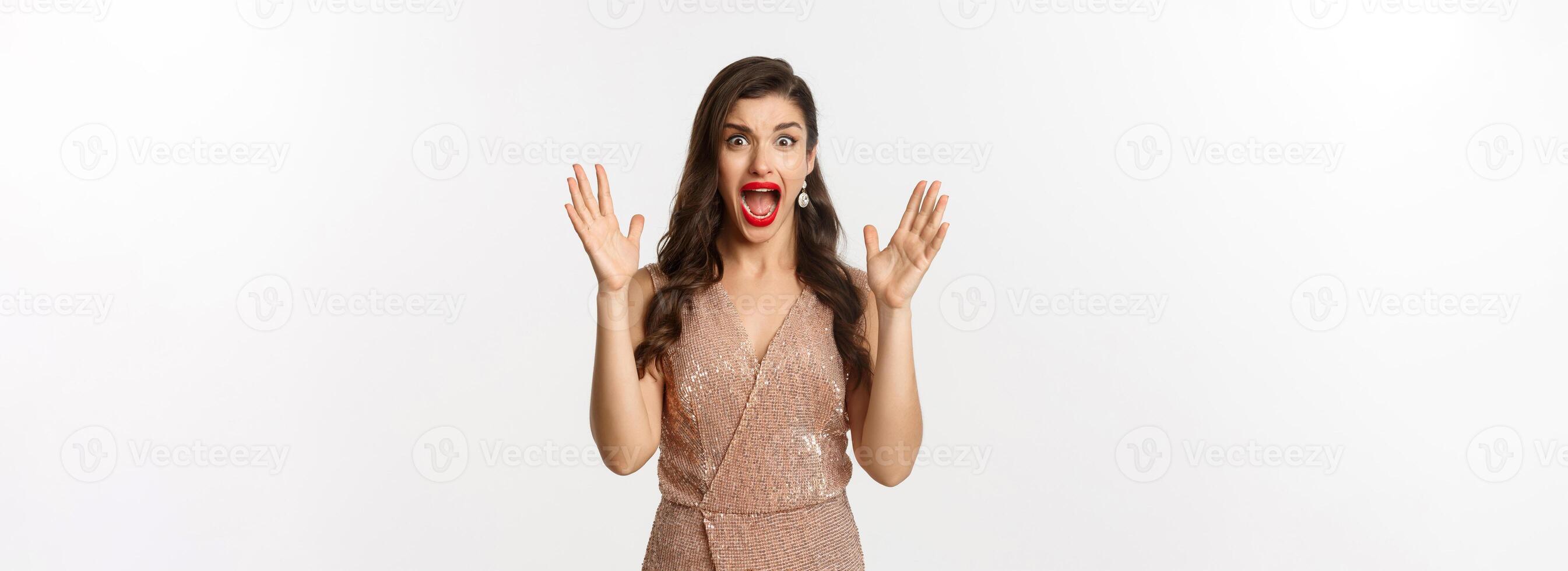 Celebration and party concept. Beautiful woman in elegant dress screaming and staring at camera scared, looking at something scary, standing over white background photo