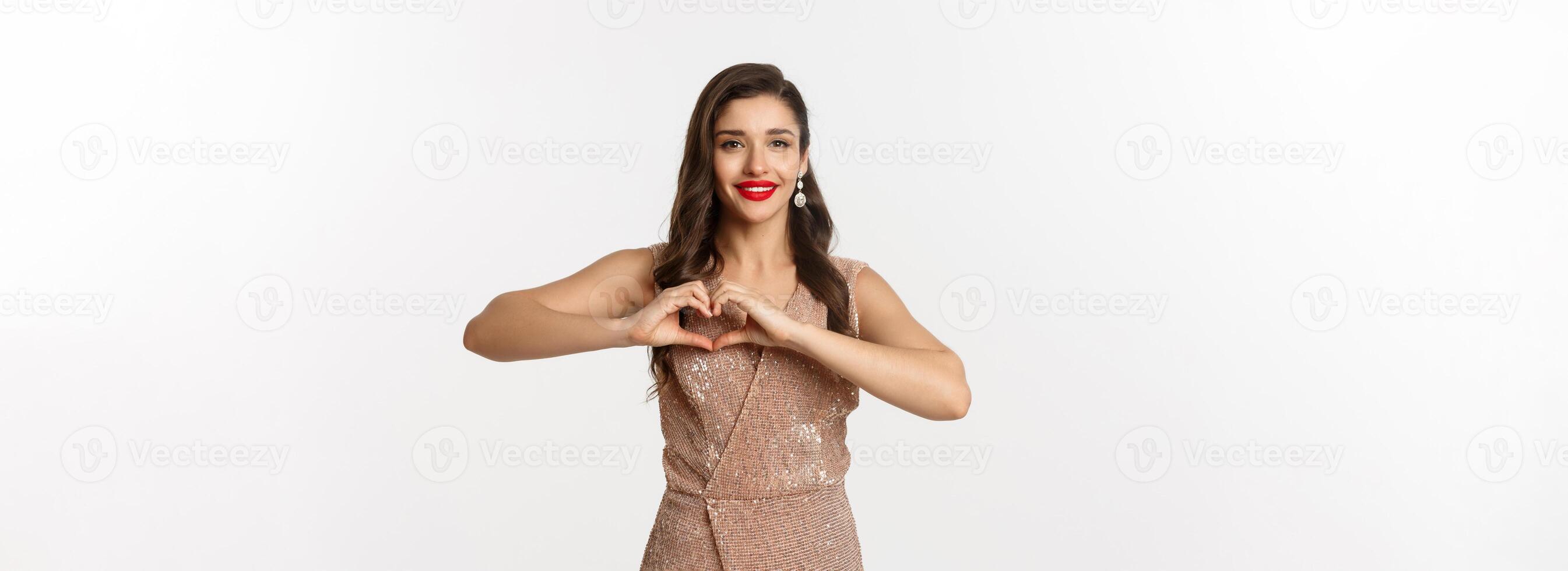 Celebration and party concept. Beautiful young woman in elegant dress showing heart sign, I love you gesture, express sympathy and smiling, white background photo