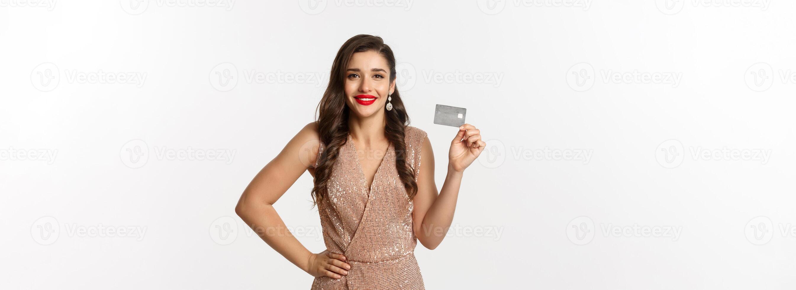 Holidays. christmas party and shopping concept. Stylish woman with red lips, glamour dress, showing credit card and smiling, standing over white background photo