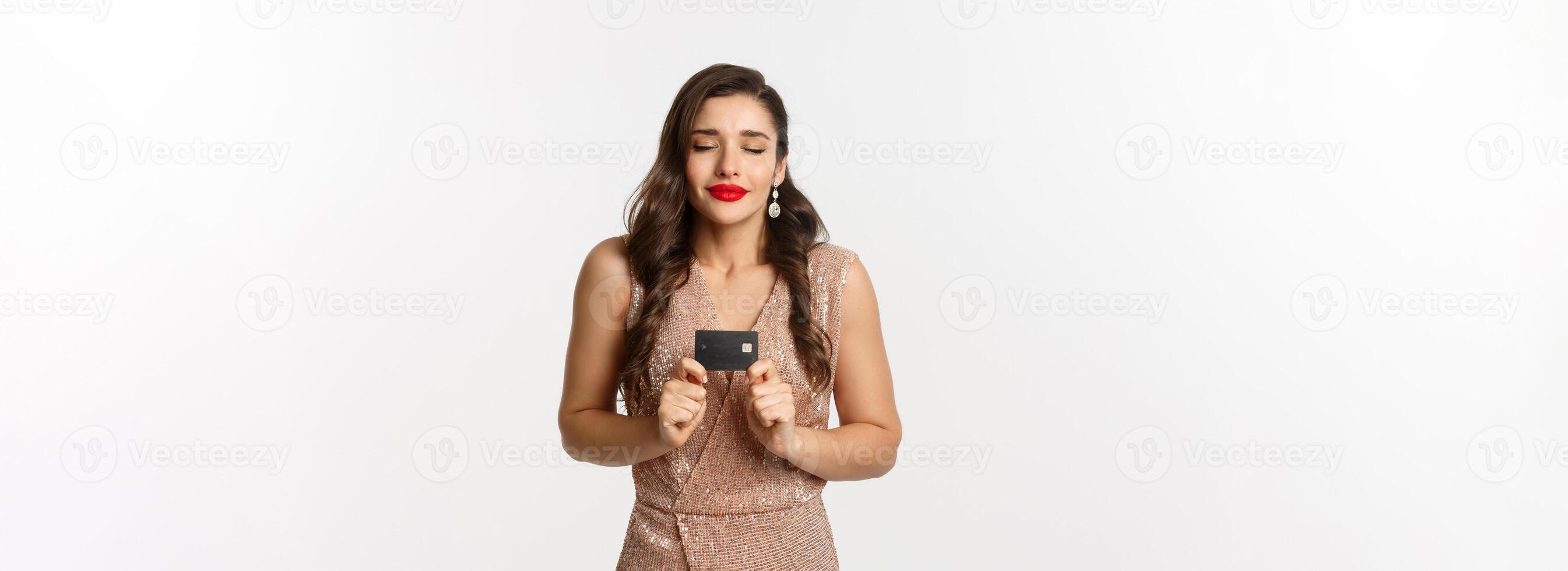 Holidays. christmas party and shopping concept. Satisfied woman in elegant dress rejoicing while showing credit card, smiling happy, standing over white background photo