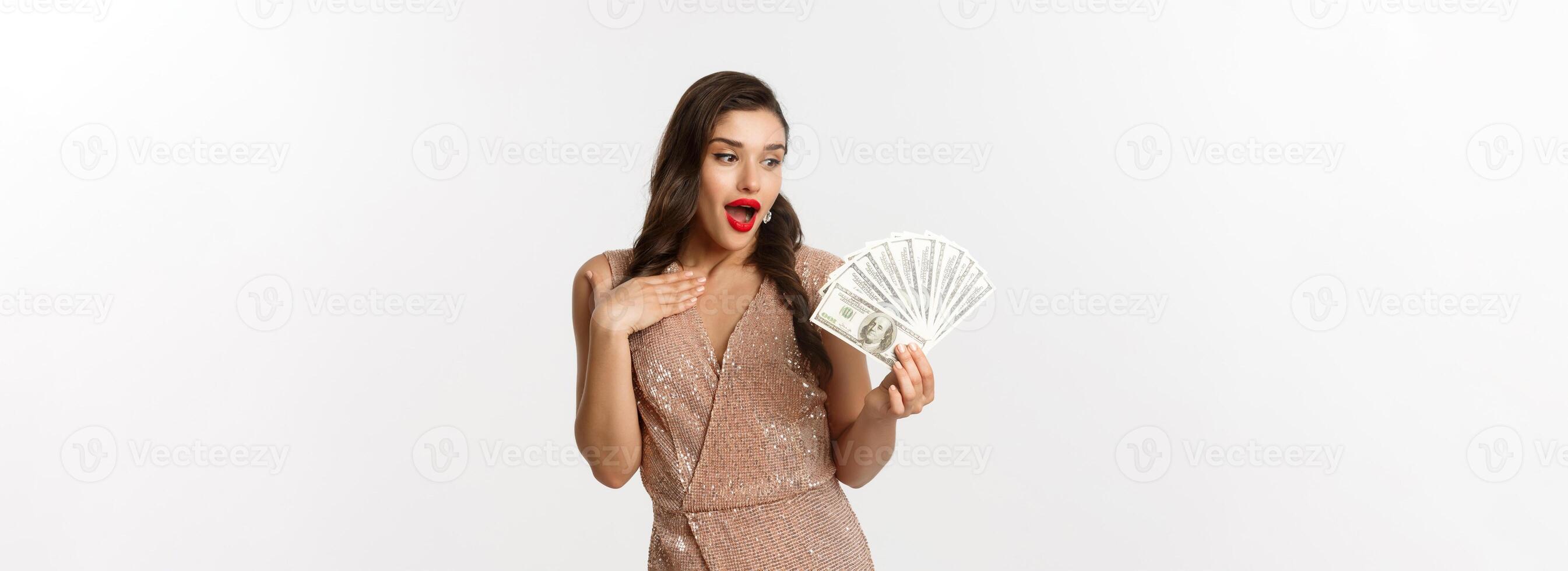 Shopping concept. Image of attractive woman in glamour dress holding money, looking at dollars with surprised face, standing over white background photo