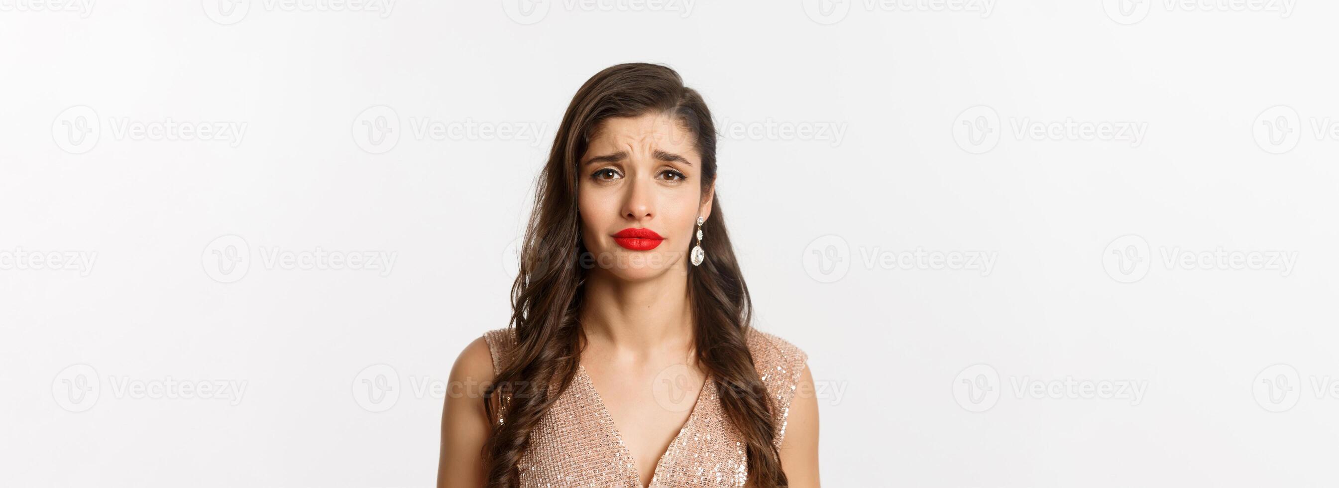 Concept of New Year celebration and winter holidays. Close-up of sad and gloomy woman with hairstyle and red lips, frowning and looking with pity, standing over white background photo