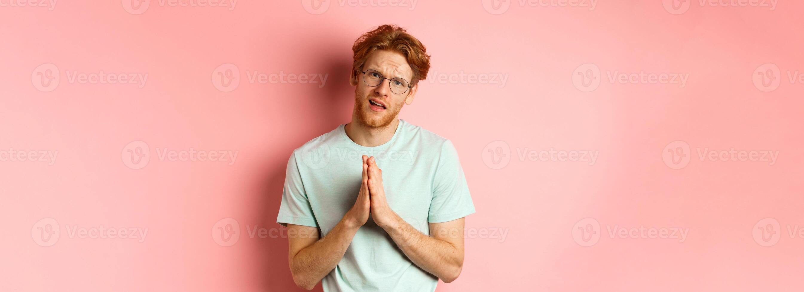 Redhead bearded guy begging for favour, holding hands in namaste gesture and asking for help, need something, standing over pink background photo