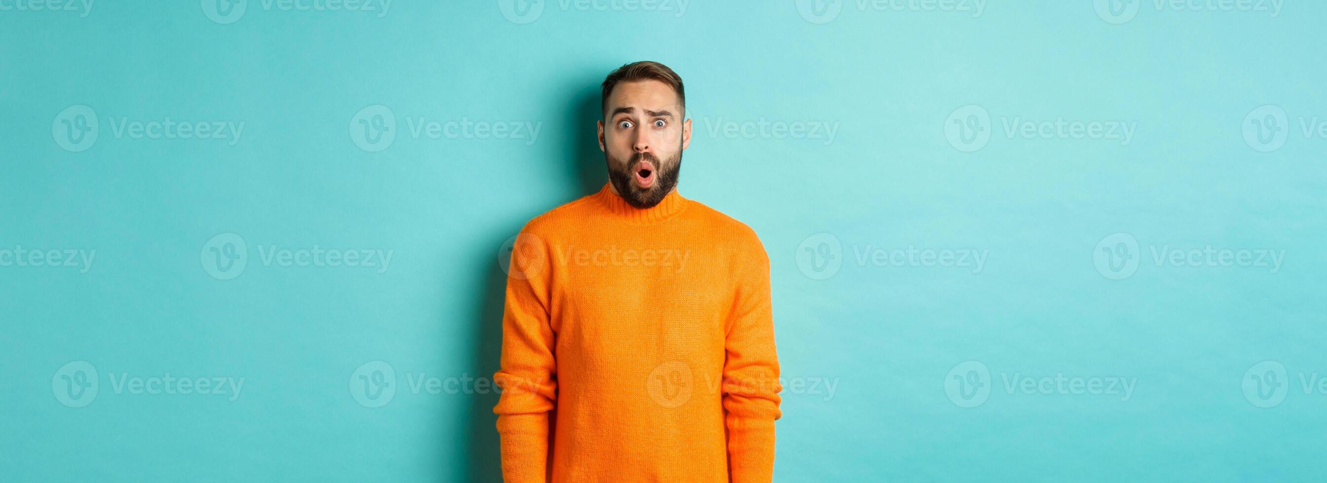 Shocked and confused man looking in awe at promo offer, standing near copy space on turquoise background photo