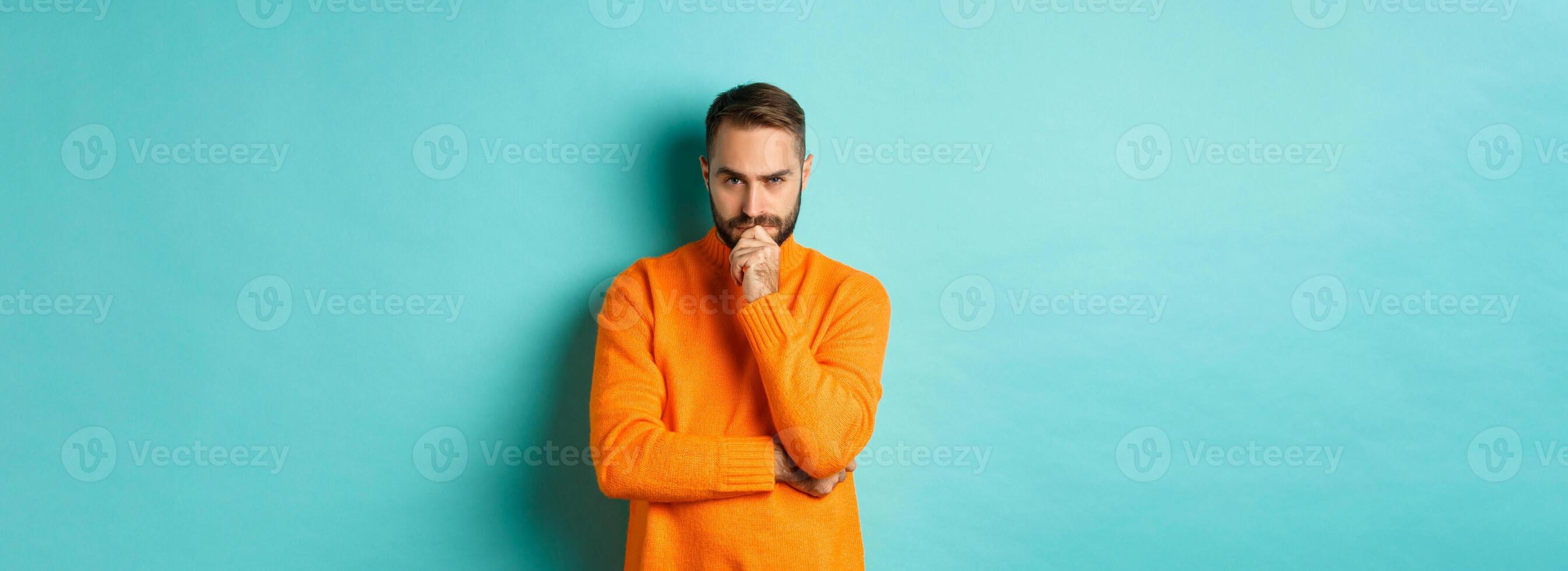 Thougtful young man making decision, looking serious and thinking, choosing, standing near copy space turquoise background photo