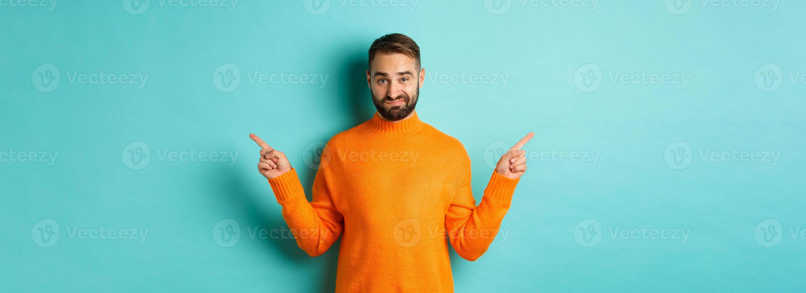 Doubtful and indecisive man pointing fingers sideways, showing different sides, two choices, looking skeptical, standing over light blue background photo