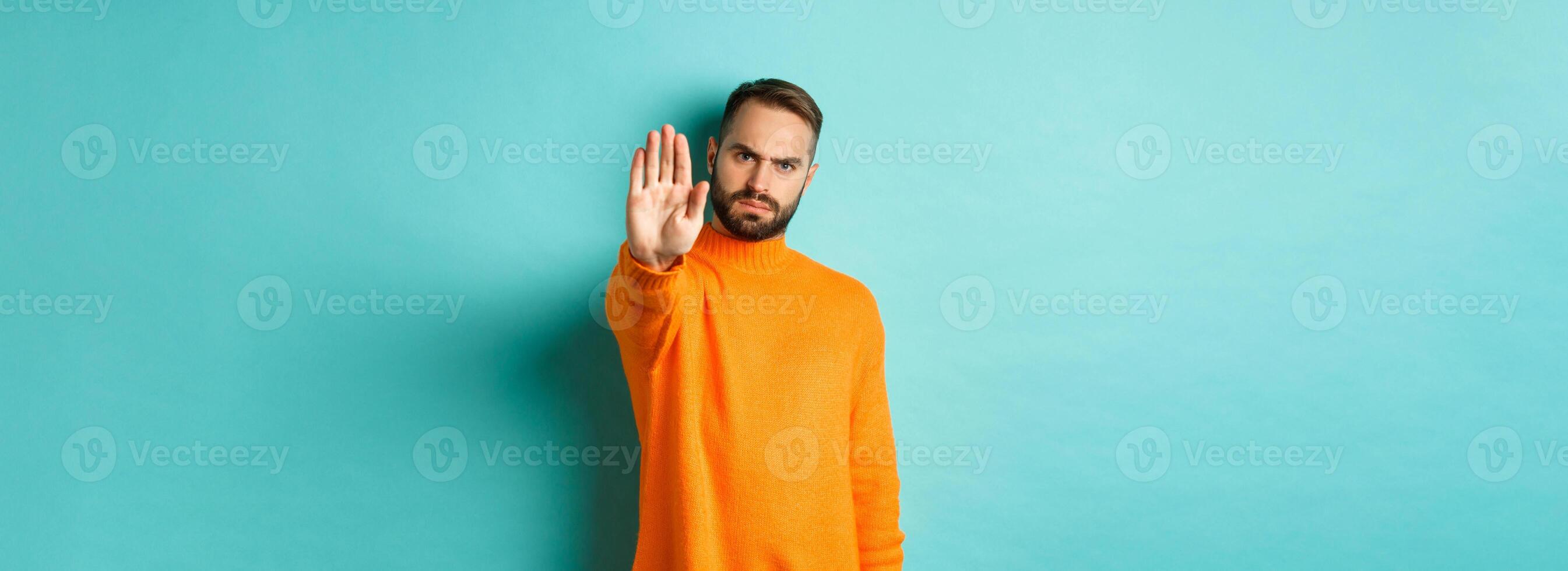 Serious frowning man showing stop gesture, telling no, prohibit and disagree, standing over light blue background photo