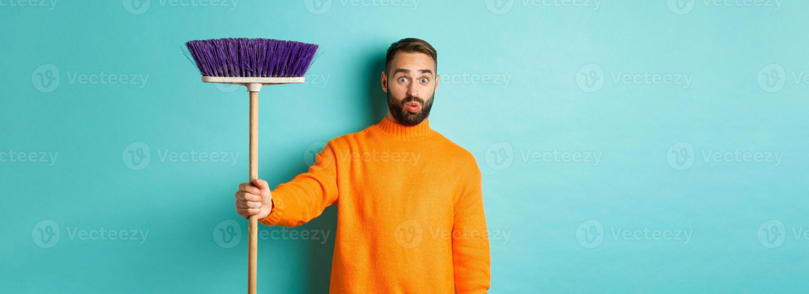 Shocked man receiving broom to do house chores, looking confused, standing over light blue background photo