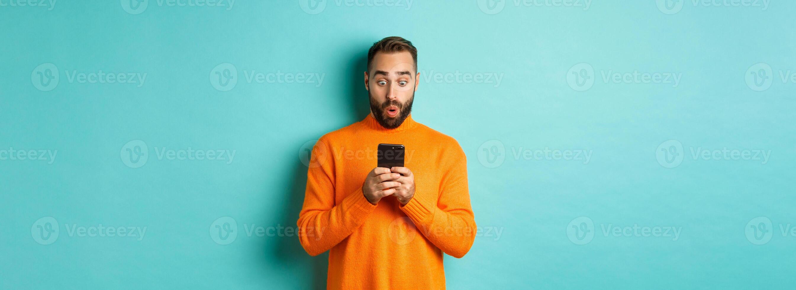 Image of man reading message with surprised face, standing amazed over light blue background photo
