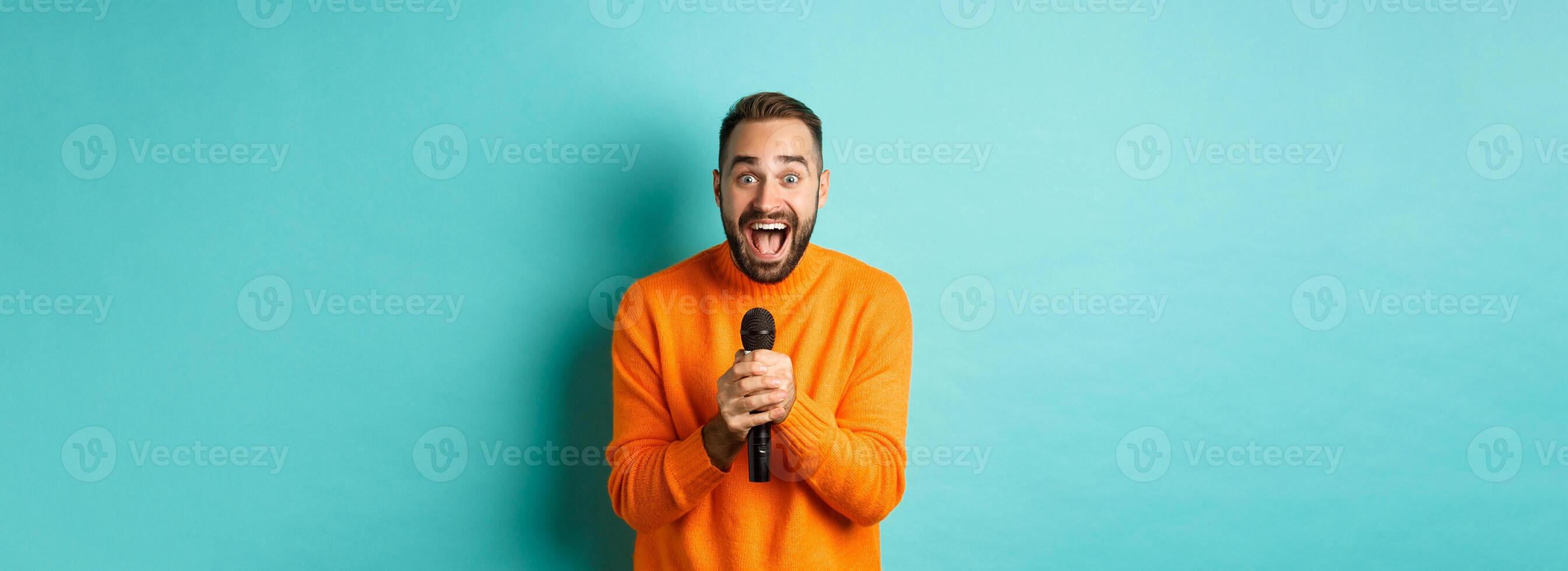 Handsome adult man perform song, singing into microphone, standing against turquoise background photo
