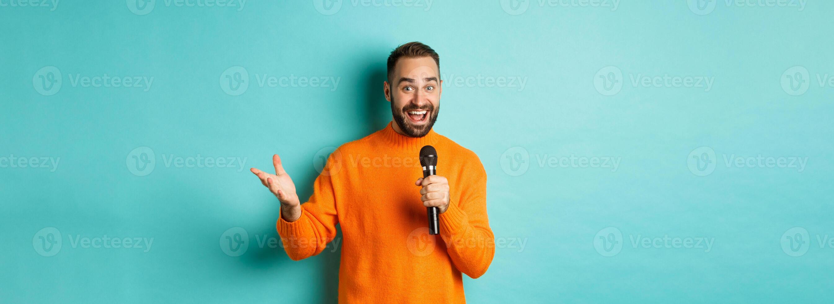 Handsome adult man perform song, singing into microphone, standing against turquoise background photo