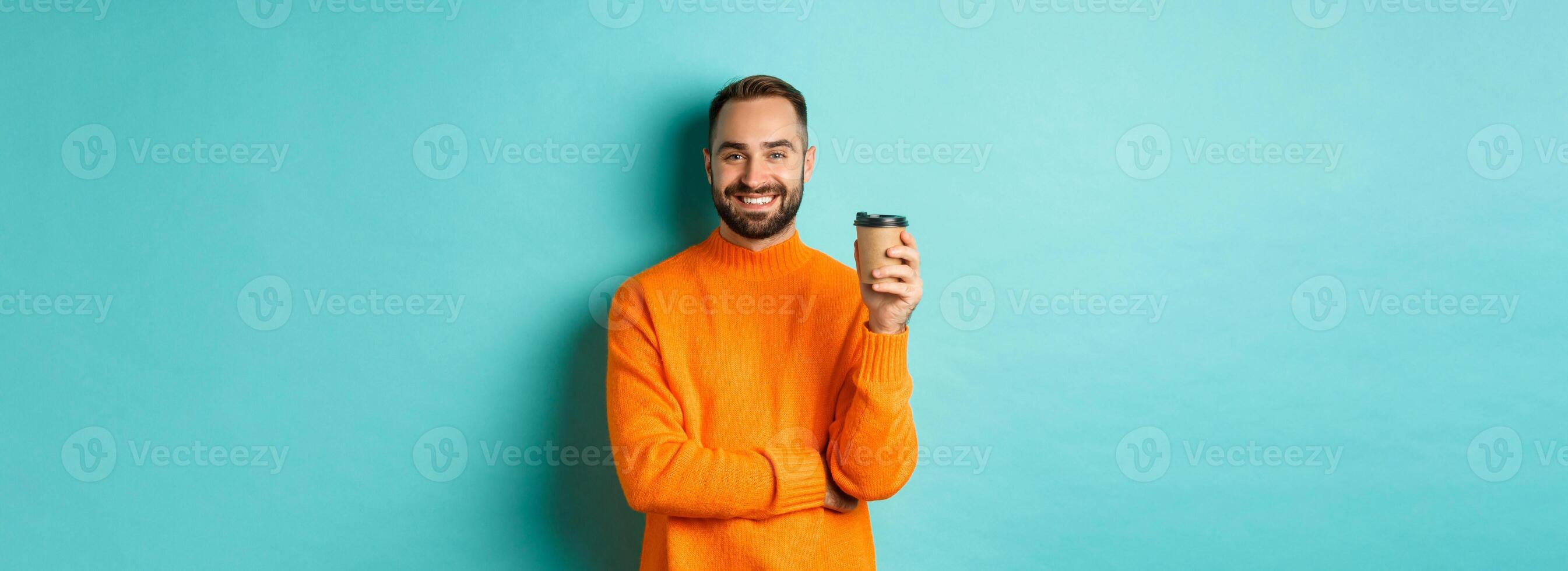 Handsome smiling man taking break, drinking coffee from takeaway, standing over blue background photo