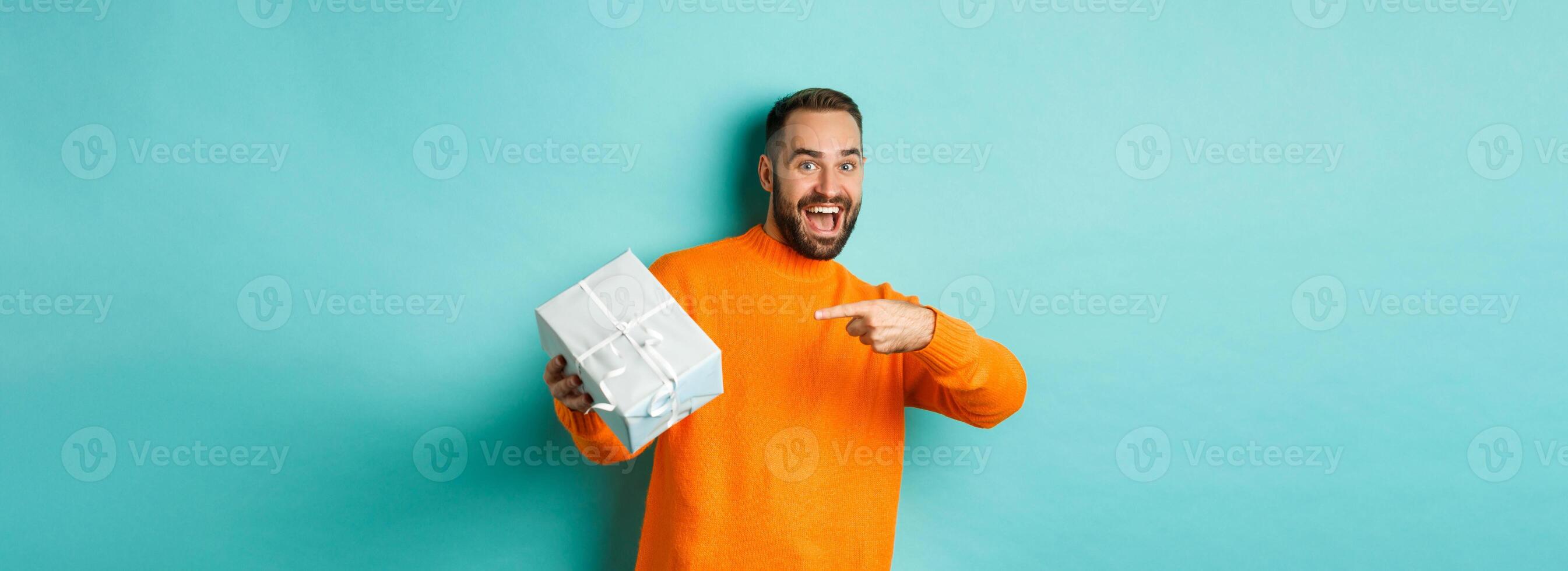 Holidays and celebration concept. Excited man receiving gift, looking happy at present and smiling, standing over blue background photo