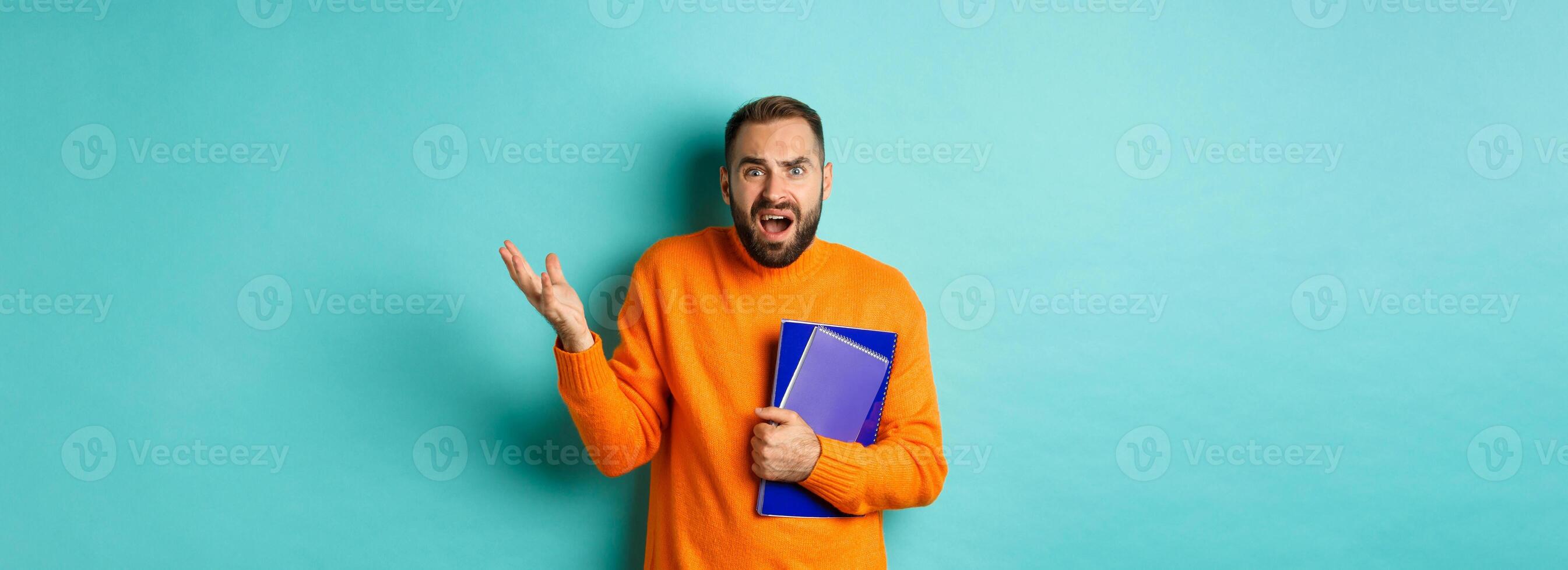 Education. Confused and disappointed man arguing, holding notebooks and complaining, standing over light blue background photo