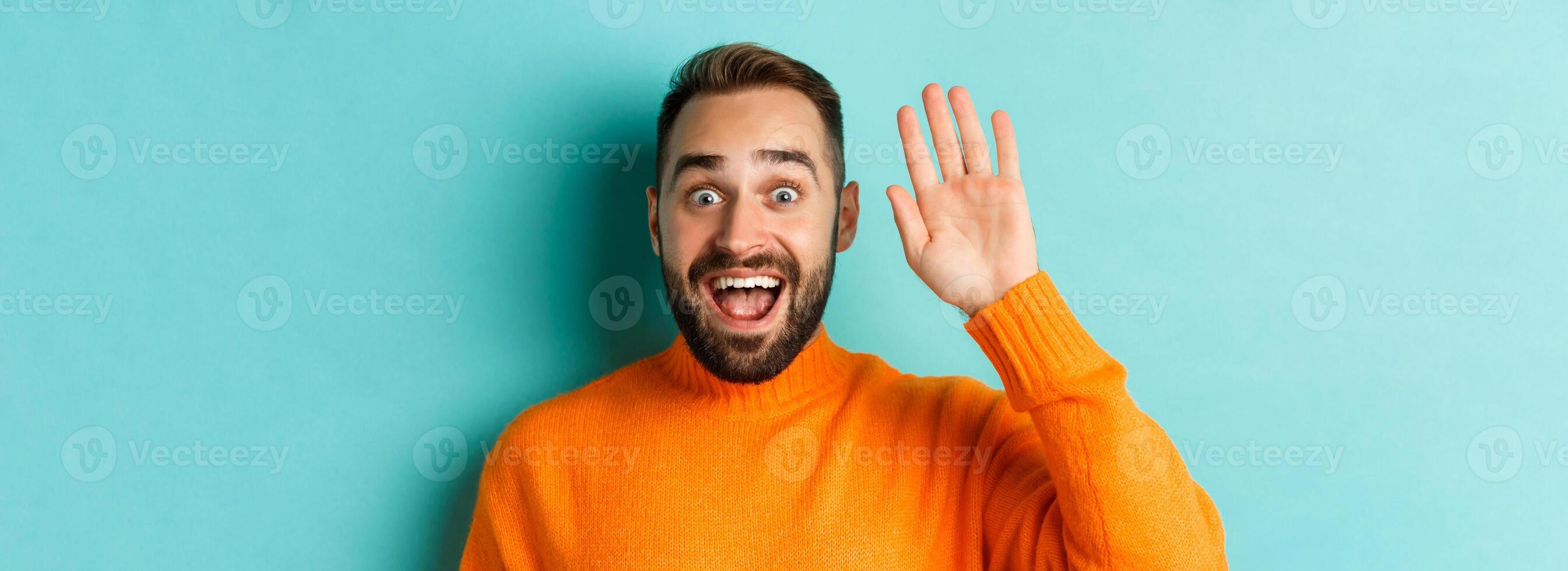 Handsome man waving hand to say hello, giving high five, standing over light blue background photo