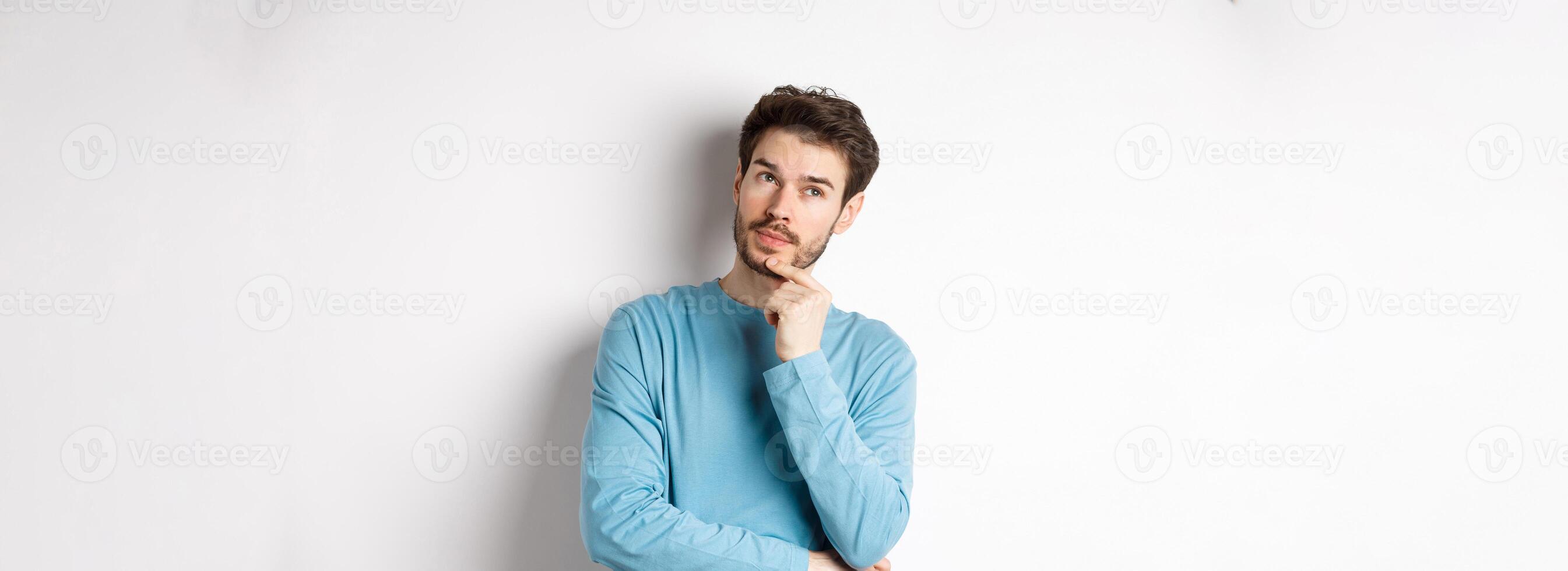 Image of handsome young man making choice, thinking and looking pensive up, standing over white background photo