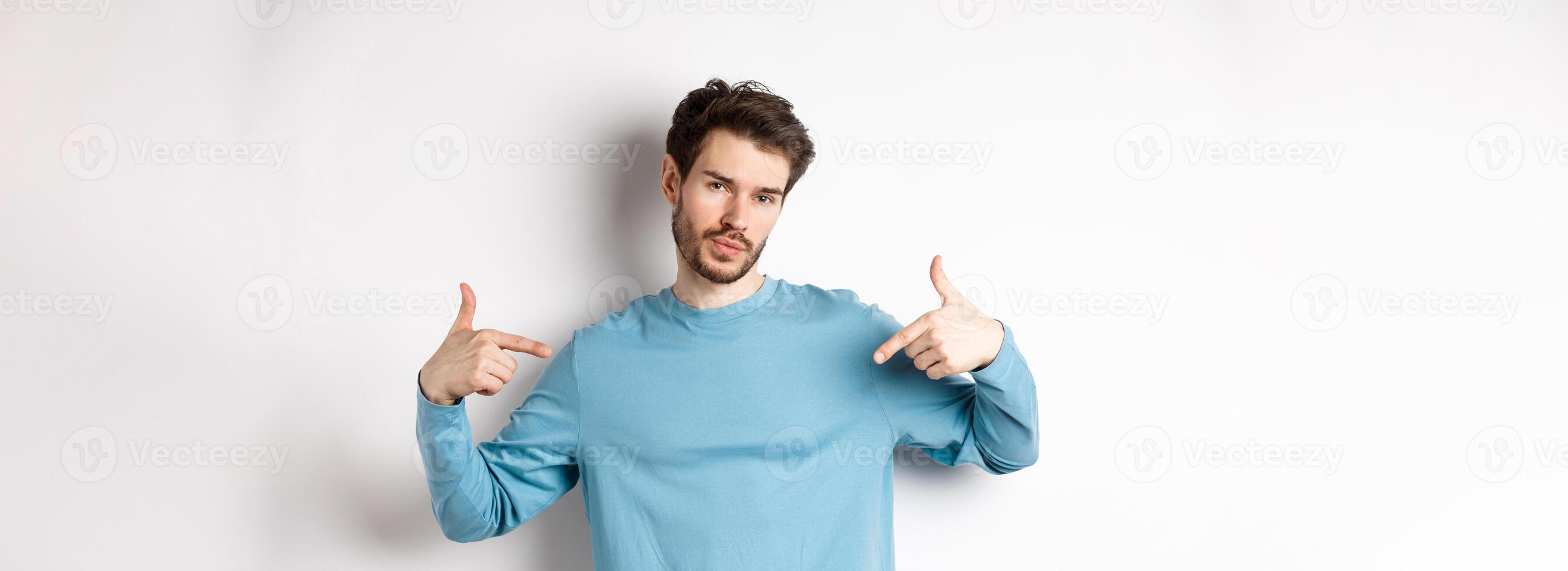 Young man with beard feeling confident, pointing at himself and making smug face, standing on white background cool and sassy photo