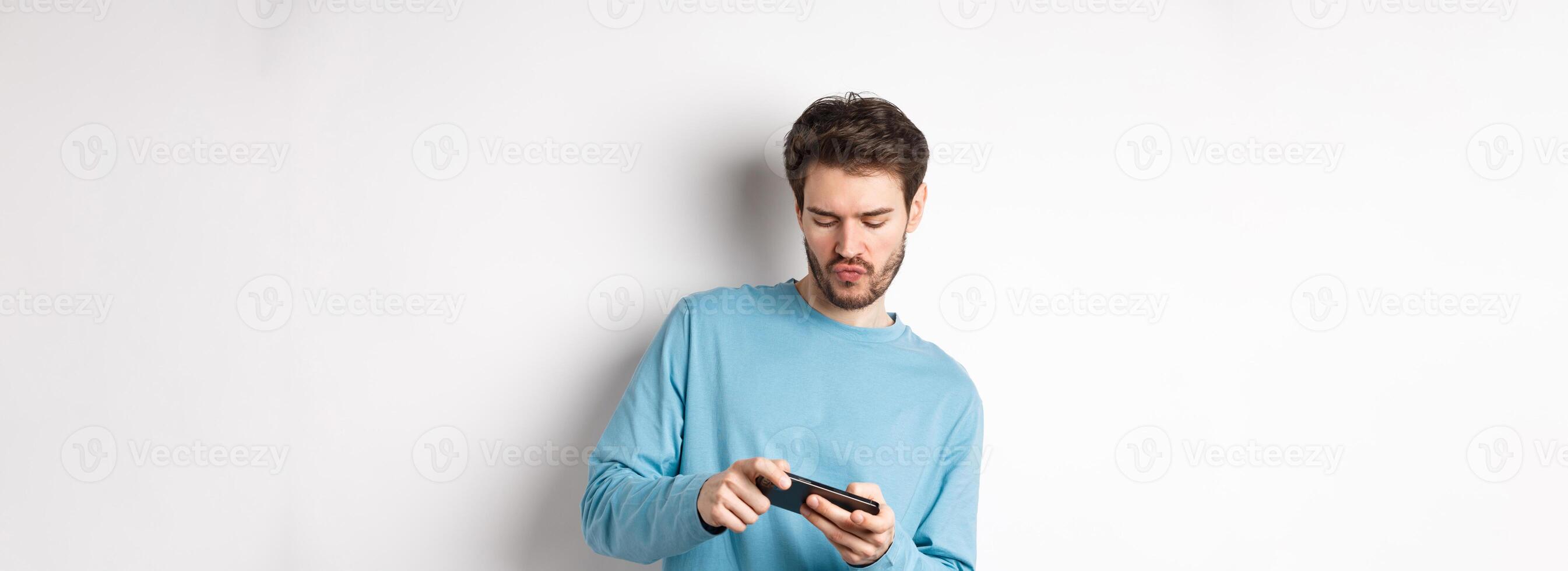 Young man playing games on smartphone, tilt body and tap mobile screen, standing joyful over white background photo