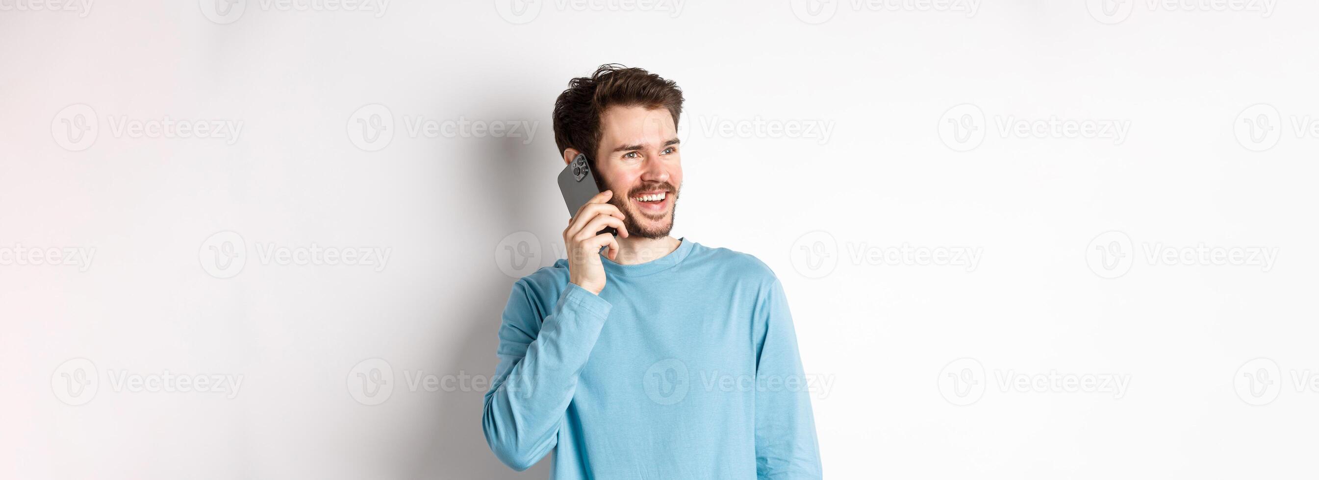 Technology concept. Joyful man enjoying phone call, talking on smartphone and smiling, standing in casual shirt over white background photo