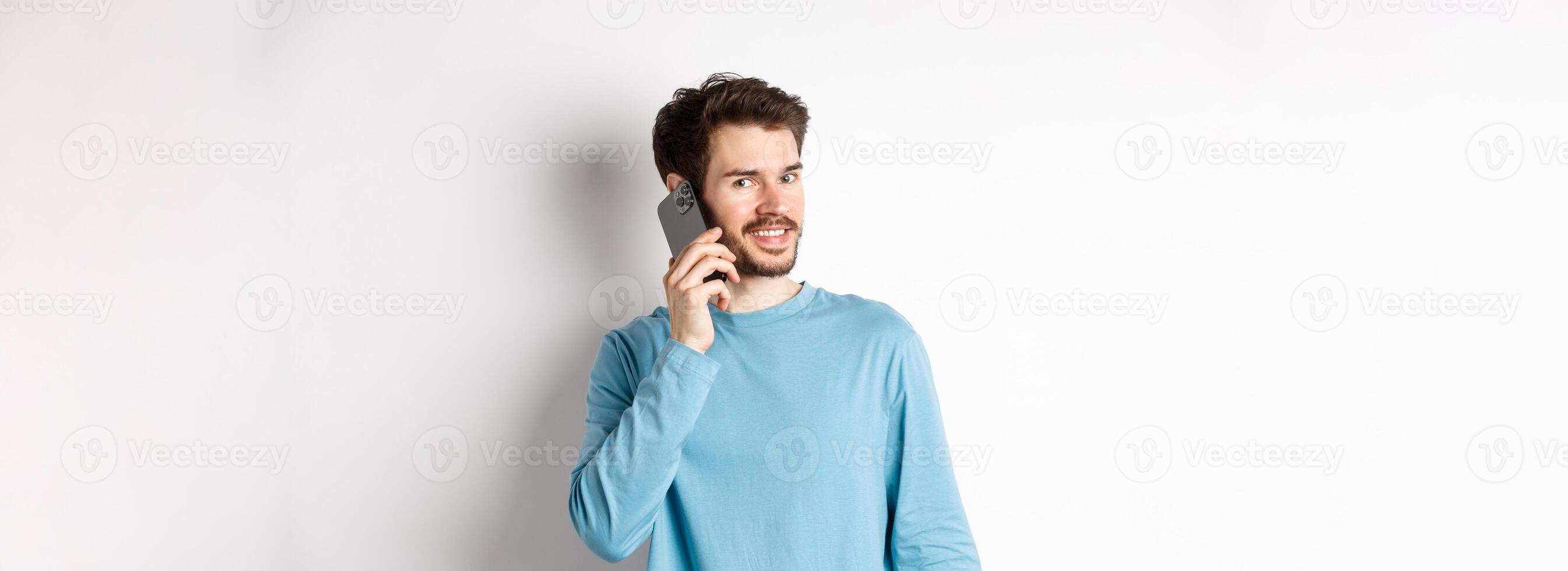 Technology concept. Young male model talking on mobile phone, calling someone on smartphone and smiling, standing over white background photo
