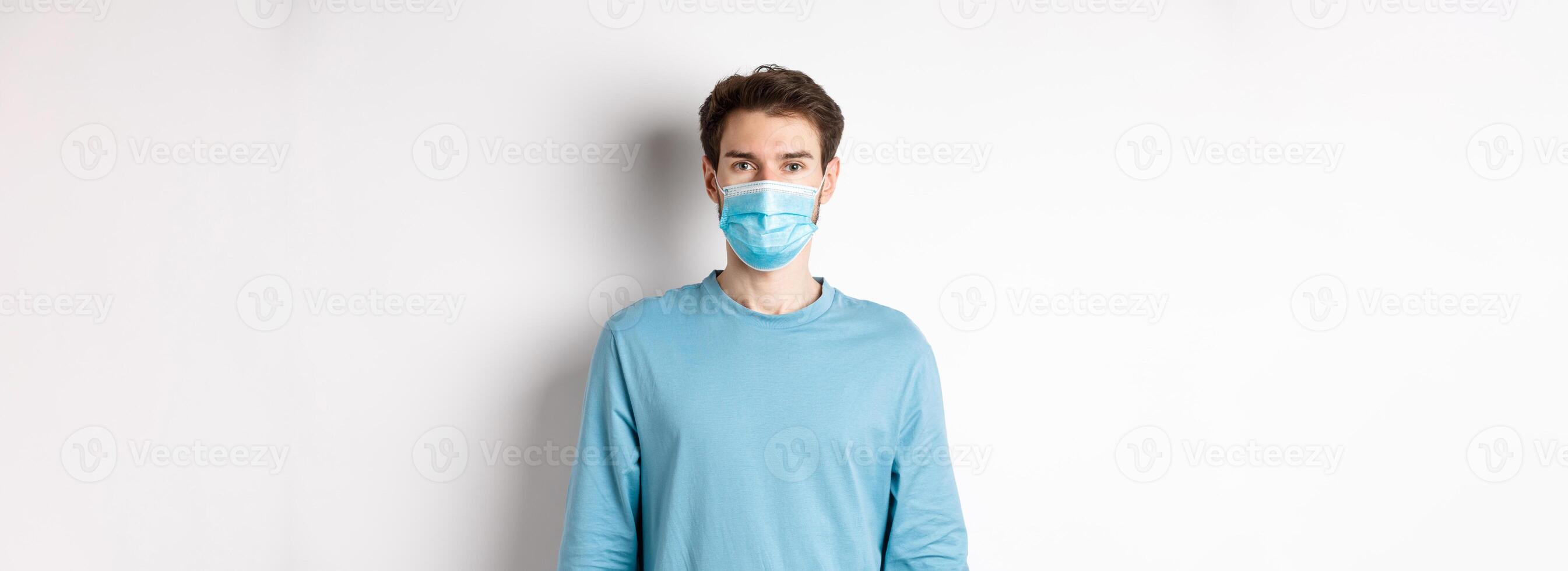 Covid-19, pandemic and social distancing concept. Young man wearing medical mask from coronavirus, standing over white background photo