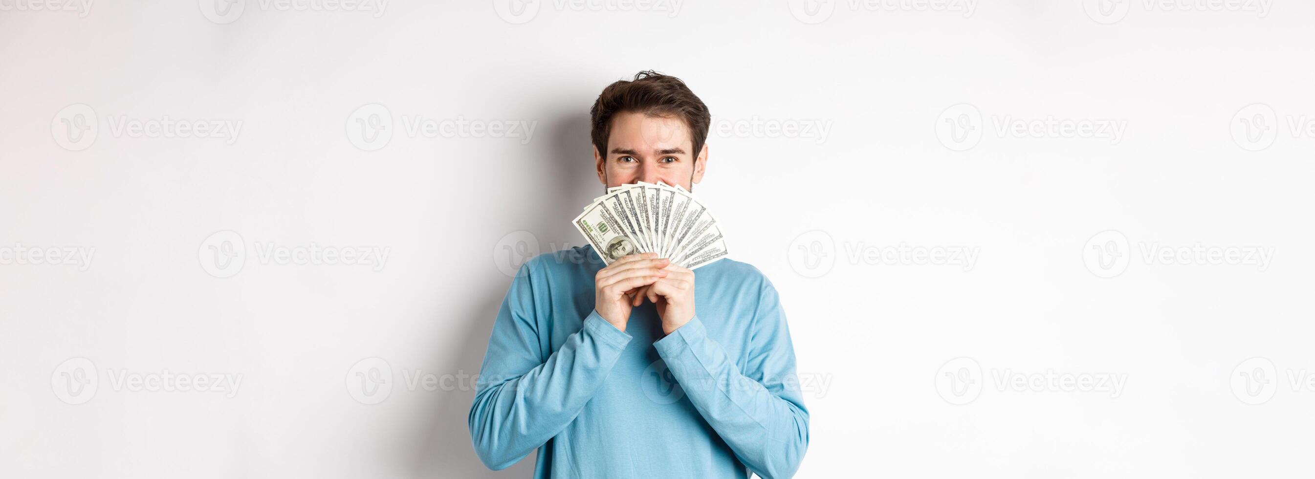 Cheerful shopper holding money for shopping, standing with dollars and smiling, standing over white background in casual clothes photo